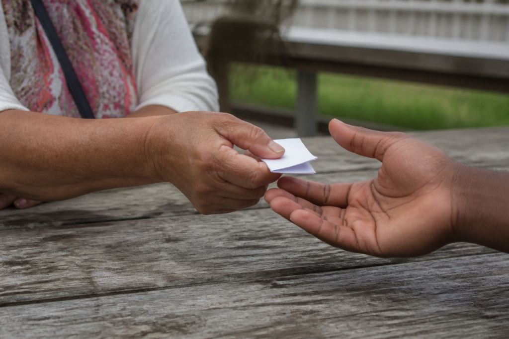 phone number for a lonely friend — one person's hand passing a folded note to another outdoors