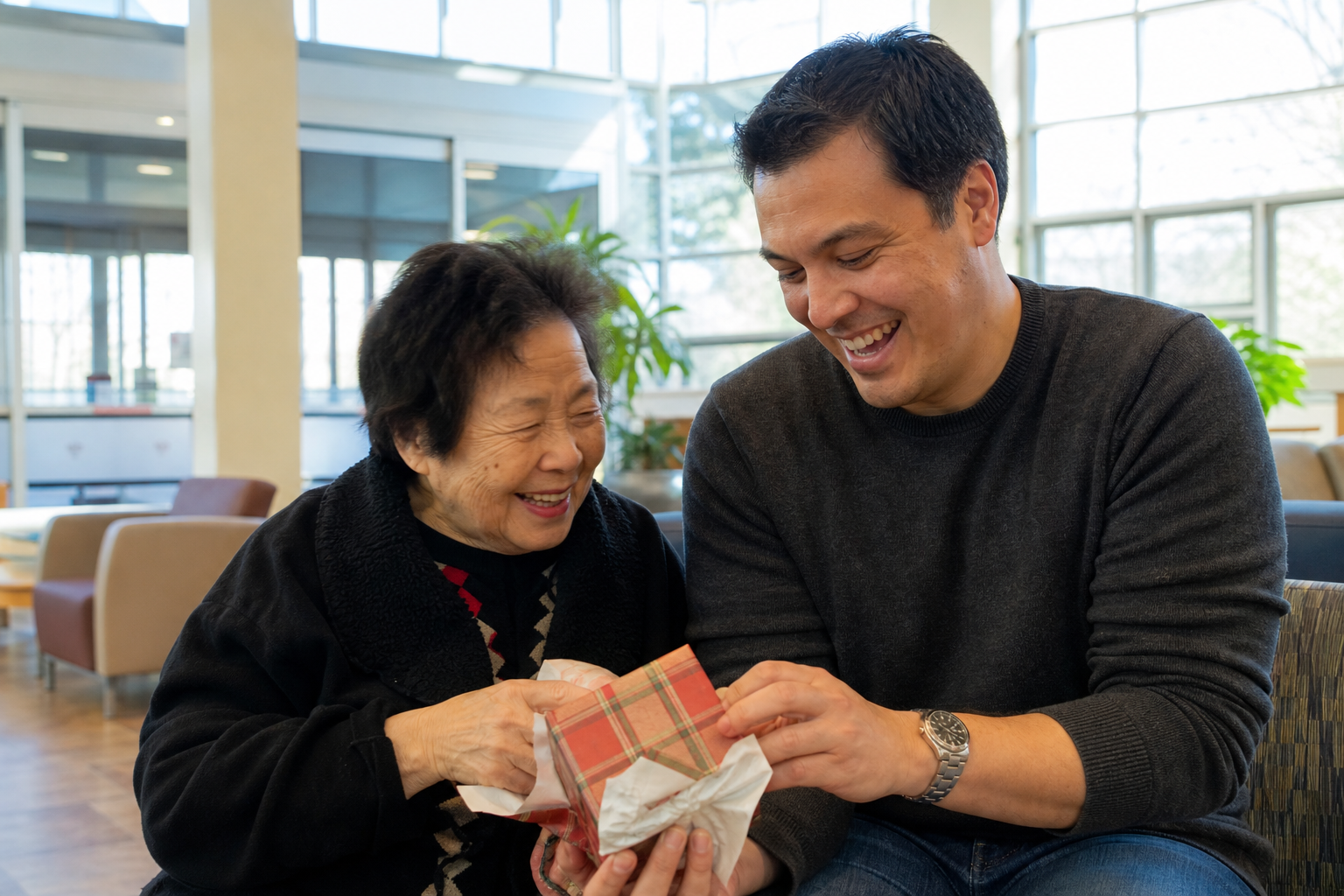 gifts for lonely seniors — a mother and her adult son laughing while unwrapping a gift together at a senior center